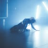 Une femme danse sur une scène. Plusieurs lumières bleues sont suspendues derrière elle.