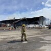 Un pompier marche devant la scène d'un feu. Un entrepôt a été complètement ravagé par les flammes. 