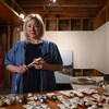 Brigitte Dion, pinceaux à la main, est debout devant ses tubes de peinture acrylique
