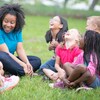 Une conseillère de camp assise sur l'herbe avec un groupe d'enfants.