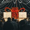 Une foule à l'extérieur pendant la nuit devant un très grand cadeau illuminé.