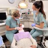 Une dentiste accompagnée de son assistante en train d'examiner les dents d'une patiente.