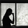 L'ombre d'une femme qui se tient la tête devant une fenêtre en noir et blanc.