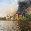 Une forêt en feu vue d'un cours d'eau.