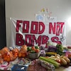 Des fruits et légumes devant une affiche Food not bombs