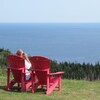 Un touriste observe la mer du haut de Cap-Gaspé, assis dans une chaise rouge.