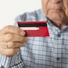 Un homme âgé parle au téléphone en tenant une carte de crédit dans son autre main.