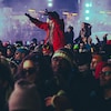 Une femme assise sur les épaules d'un homme parmi une grande foule qui assiste à un spectacle extérieur en hiver.