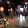 Quatre participants, dont un en fauteuil roulant, à un match d'improvisation sur une scène.