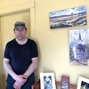 Joël Deveau debout dans un bureau est entouré d'oeuvres d'art accrochées au mur.