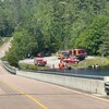 Des véhicules et du personnel du service de sécurité incendie en bordure d'un lac et d'une route dans une forêt.