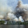 Une forêt en flamme et en fumée vue d'un lac.