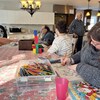 Des adultes utilisent des livres à colorier et des blocs, assis à une grande table. 