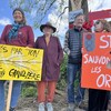 Des gens, pancartes en main, manifestent devant d'immenses arbres. 