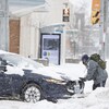 Un homme pousse une voiture enlisée dans la neige.