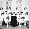 Six jeunes infirmières tenant un bouquet de fleurs entourent une religieuse.