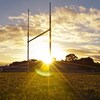 Un poteau de but sur un terrain de football et de rugby au coucher du soleil.