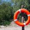 Une bouée de sauvetage accrochée sur un poteau de bois sur le bord d'une plage.
