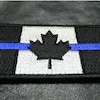 Un écusson du drapeau du Canada en noir et blanc traversé par une bande horizontale bleue.