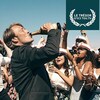 Un homme (Mads Mikkelsen) boit une bouteille de champagne au goulot, au milieu d'une foule hilare.