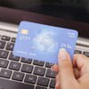Une femme devant un clavier d'ordinateur tient une carte de crédit dans la main. 