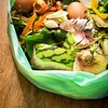 Sur une table en bois, un sac de plastique vert est rempli de résidus alimentaires.