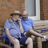 Deux hommes assis sur un banc se prennent dans leurs bras.
