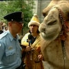 Jean-René Dufort déguisé en roi mage tient un chameau et un micro devant un policier de la ville de Montréal.