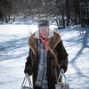 Une vieille femme (Martin Villeneuve) portant des sacs d'épicerie marche dans la neige.