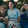 Trois jeunes filles souriantes, assises sur un banc de parc.