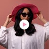 Jemmy Echaquan Dubé sourit en portant des lunettes de soleil et un chapeau devant un arrière-plan, à côté d'un bouton «Jouer» et le logo de la Minute MAJ.
