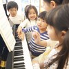 Five children and an adult are around a piano and playing the notes.