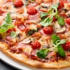 Une pizza à croute mince qui contient des tomates, du basilic, du fromage et du prosciutto.