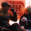 Un vieil homme et une petite fille assis par terre, sous la neige, devant la vitrine d'un commerce, éclairée au néon rouge.