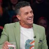 Il est assis en studio et il rit.