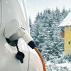 Une voiture électrique branchée à un câble de recharge. C'est l'hiver.