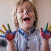 Le petit garçon d'environ 4 ans rit en montrant ses mains pleines de peinture