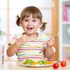Une petite fille qui porte des couettes sourit en mangeant des légumes