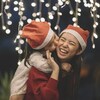 Une maman et sa fille, d'origine asiatique, portent des bonnets de Noel et rient en se faisant un câlin