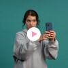 Livia Martin prend un selfie devant un arrière-plan, à côté d'un bouton «Jouer» et le logo de la Minute MAJ.