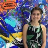 Mégane Fortin devant une murale d'art abstrait, avec le collant de la Bonne Nouvelle de MAJ.