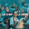 Dans un désordre tumultueux s'entrecroisent des cuisinier, serveurs, instruments de cuisine, factures et commandes. Au milieu du chaos, une cheffe lève le regard, une commande à la main.