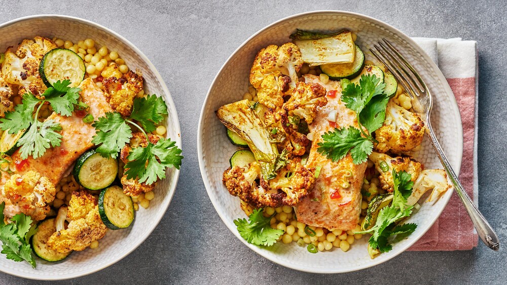 Deux bols remplis de couscous israélien, de saumon et de chou-fleur rôti.