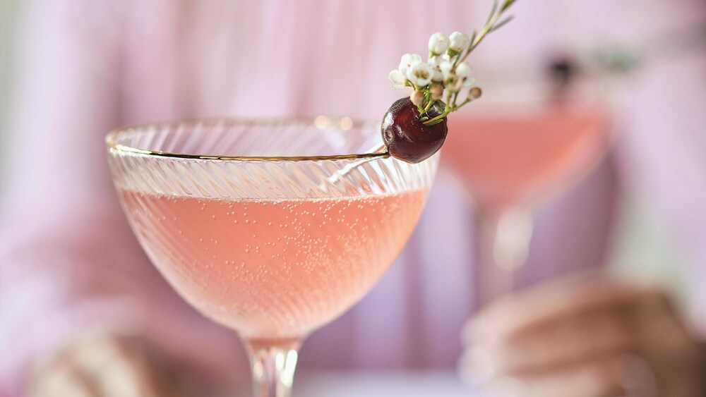 Un cocktail au jasmin et à la cerise décoré d'une cerise et de petites fleurs.
