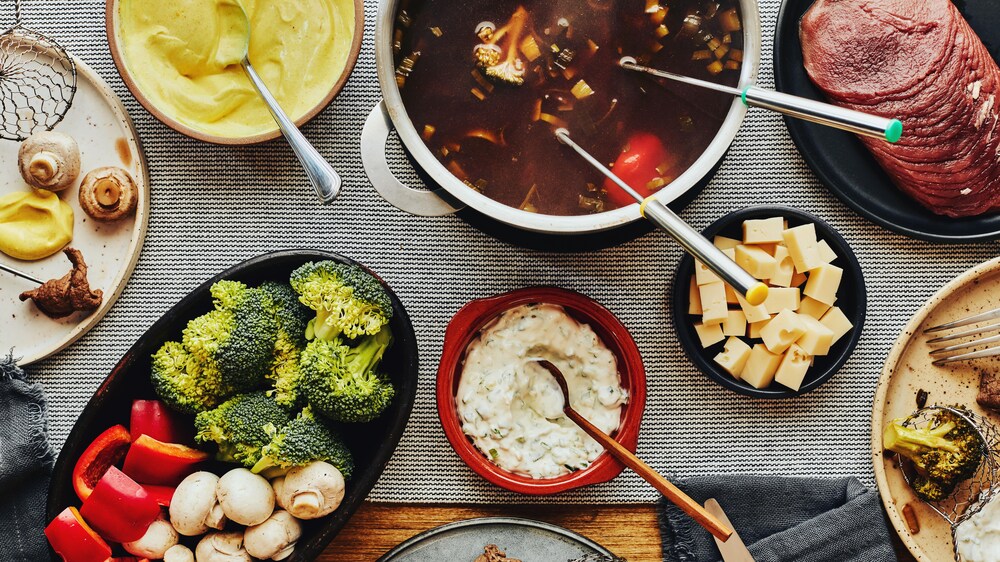 Sur une table, est déposé plusieurs plats de services, dont le pot contenant le bouillon à fondue chinoise.