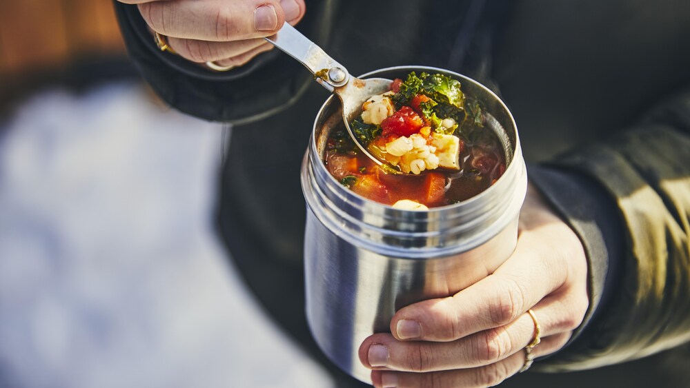 Une personne tient dans ses mains un thermos remplit de soupe.
