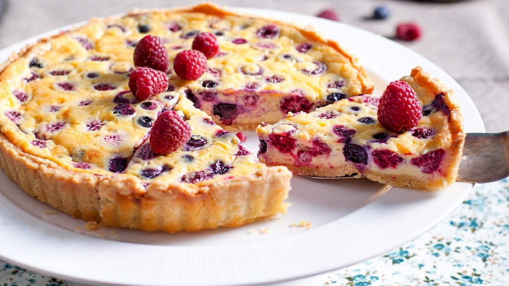 Une tarte aux amandes et aux petits fruits sur un présentoir à gâteau en train d'être coupée en morceaux.