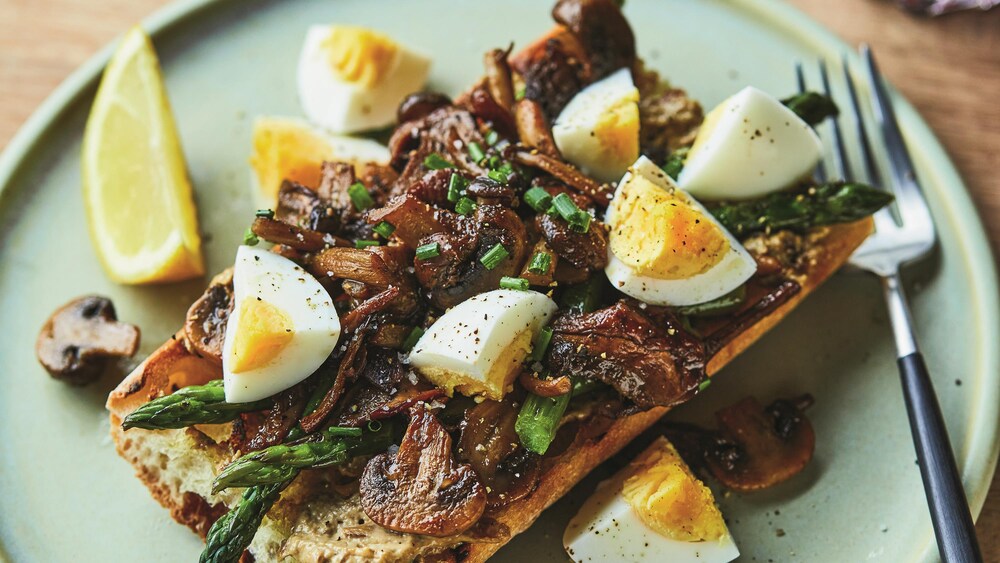 Une tartine de champignon servie avec des morceaux d'œuf cuit dur et des asperges.