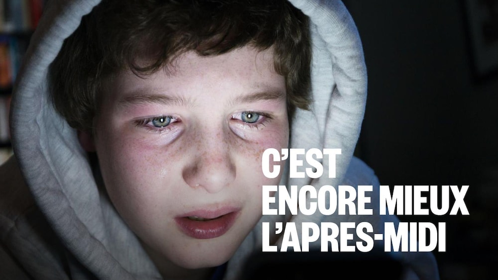Un garçon dans la pénombre et son visage est éclairé par son appareil.