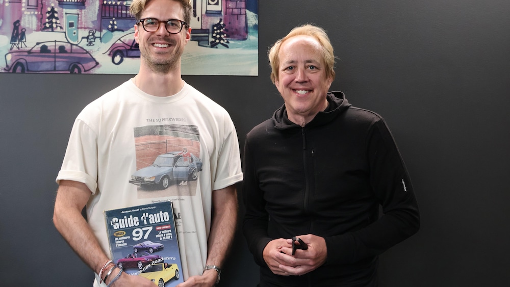 Julien Poirier-Malo a le Guide de l'auto 97 dans les mains, accompagné de l'auteur de ce guide, le chroniqueur automobile Gabriel Gélinas. Les deux personnes sont souriantes. 